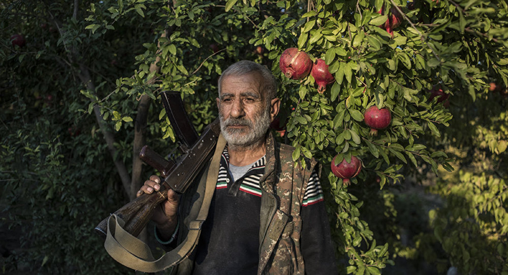 A local resident Anushavan (62) stands in a pomegranate garden in the yard of his house. He is holding an old Kalashnikov assault rifle, which he has kept from the first Karabakh war.  Ukhtasar village.